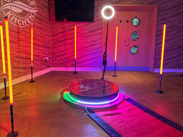 A photo booth setup with lights and a red carpet, surrounded by decorative ropes and balloons.
